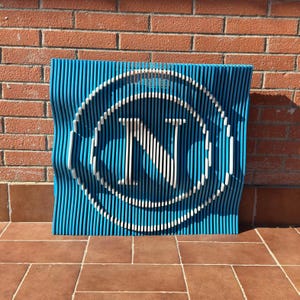 Könnte beinhalten: Ein blaues und weißes Wandkunstwerk aus Holz mit einem stilisierten Buchstaben N in einem Kreis. Das Stück besteht aus dünnen Holzlatten, die in Wellenform angeordnet sind.