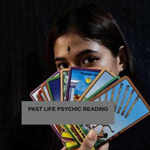 May include: A fan of colorful tarot cards held up, featuring illustrations of wands, a moon, and architectural columns. A grey rectangular overlay displays the black text PAST LIFE PSYCHIC READING across the center of the deck of cards.