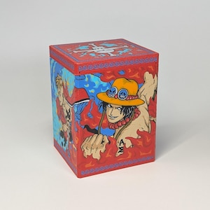 Könnte beinhalten: Eine rot-blaue Box mit Anime-Charakteren. Die Box hat einen roten Deckel mit blauem Rand und einem weißen Emblem. Die Seiten der Box zeigen Illustrationen von Anime-Charakteren auf einem feurigen Hintergrund.