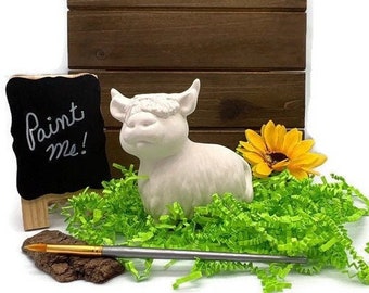 Peut inclure: Figurines de vache écossaise en céramique blanche avec un panneau "peignez-moi". La vache est assise sur de l'herbe verte avec un tournesol jaune.