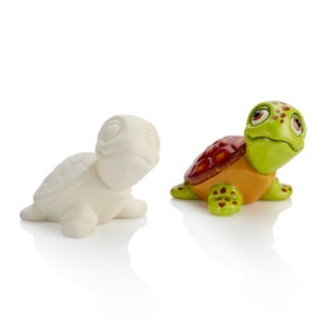May include: A painted ceramic turtle figurine with a green shell, orange belly, and red markings. The turtle has large eyes and a friendly expression. A plain white ceramic turtle figurine is also shown.