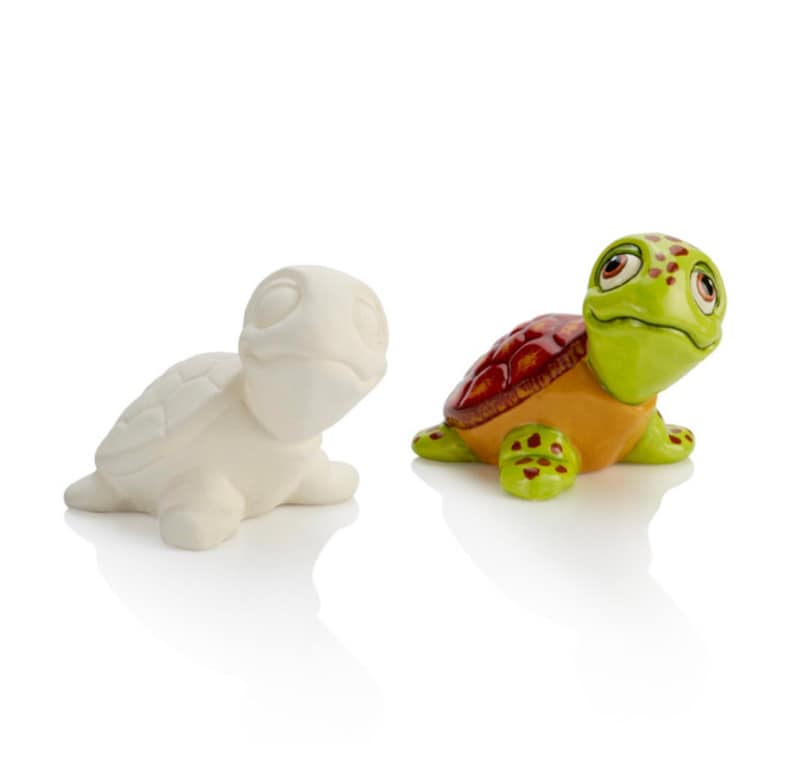 May include: A painted ceramic turtle figurine with a green shell, orange belly, and red markings. The turtle has large eyes and a friendly expression. A plain white ceramic turtle figurine is also shown.