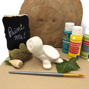 May include: A white ceramic turtle figurine with a paint me sign, paintbrushes, and three bottles of acrylic paint in blue, yellow, and green.