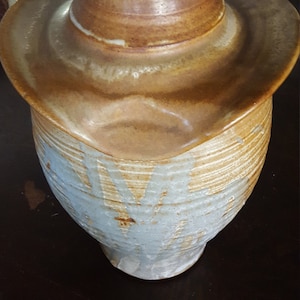 May include: A ceramic vase with a wide, flared opening and a brown and white glaze. The vase has a unique, organic shape and a textured surface.