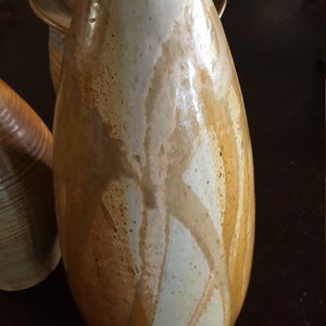 May include: A handmade ceramic vase with a teardrop shape. The vase has a light beige base with streaks of brown and white glaze. The vase is approximately 10 inches tall.