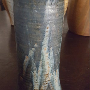 May include: A blue and brown ceramic vase with a unique, abstract design. The vase has a textured surface and a slightly curved shape.