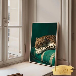 May include: A framed art print featuring a sleeping leopard with a spotted coat, resting on a green and white striped cushion. The artwork is set against a dark green background, with a wooden frame. The print is displayed on a windowsill.