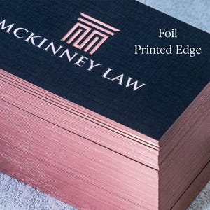 May include: A stack of business cards with a navy blue top and rose gold edges. The cards feature the text "MCKINNEY LAW" in white, with a rose gold logo. The words "Foil Printed Edge" are also visible.
