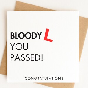 May include: A square white greeting card with black text that reads BLOODY L YOU PASSED! with a large red letter L. Below this, the word CONGRATULATIONS is printed in black. The card is positioned against a plain light brown envelope background.
