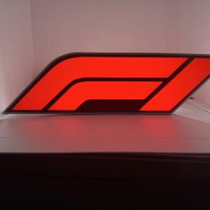 May include: A red and black Formula 1 logo, a stylised letter F, is displayed on a white surface.