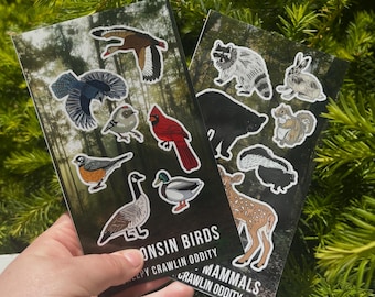 May include: Two illustrated cards featuring wildlife stickers. One card displays bird stickers, including a cardinal and a robin. The other card shows mammal stickers, such as a raccoon and a deer. The cards have a forest background and text that reads "Wisconsin Birds" and "Wisconsin Mammals".