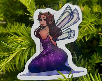 May include: A die-cut sticker featuring an illustration of a fairy with brown hair and pointed ears, wearing a purple dress with a white star-speckled pattern. The fairy has translucent blue-tinted wings and is kneeling on a purple base.