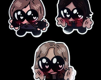 May include: Three die-cut stickers featuring cartoon characters with large black eyes containing white heart highlights. The characters have light brown or dark brown hair, blush on their cheeks, and are wearing casual clothing in shades of brown, red, and black.