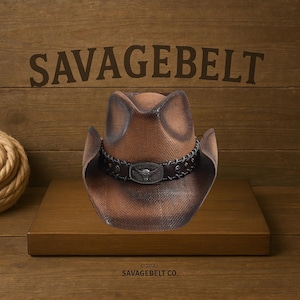 Op de afbeelding: Een bruine cowboyhoed met een verweerde look en een zwarte leren band met een metalen gesp met een schedelontwerp. De hoed ligt op een houten oppervlak met de tekst "SAVAGEBELT" erboven en "©2022 SAVAGEBELT CO." eronder.