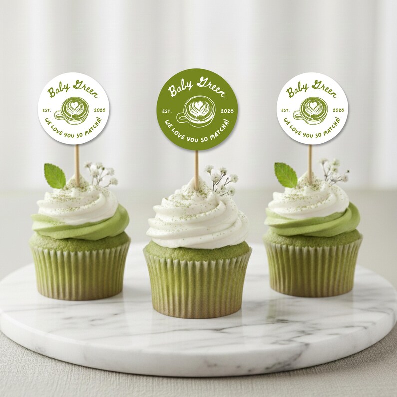 May include: Three matcha cupcakes with white frosting and green buttercream swirls, topped with decorative Baby Green toppers. Each cupcake has a sprig of baby's breath and a mint leaf. The toppers read "Baby Green" and "We love you so matcha!"