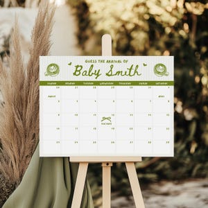 May include: A white calendar on an easel with the text "GUESS THE ARRIVAL OF Baby Smith." The calendar has a green border and a calendar grid with the month of March and April. The due date is marked on the 12th.