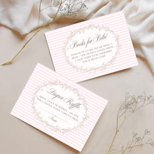 May include: Two baby shower cards with pink and white stripes. One card reads "Books for Bebé" and the other says "Diaper Raffle". Both cards have floral wreath designs and space for writing.