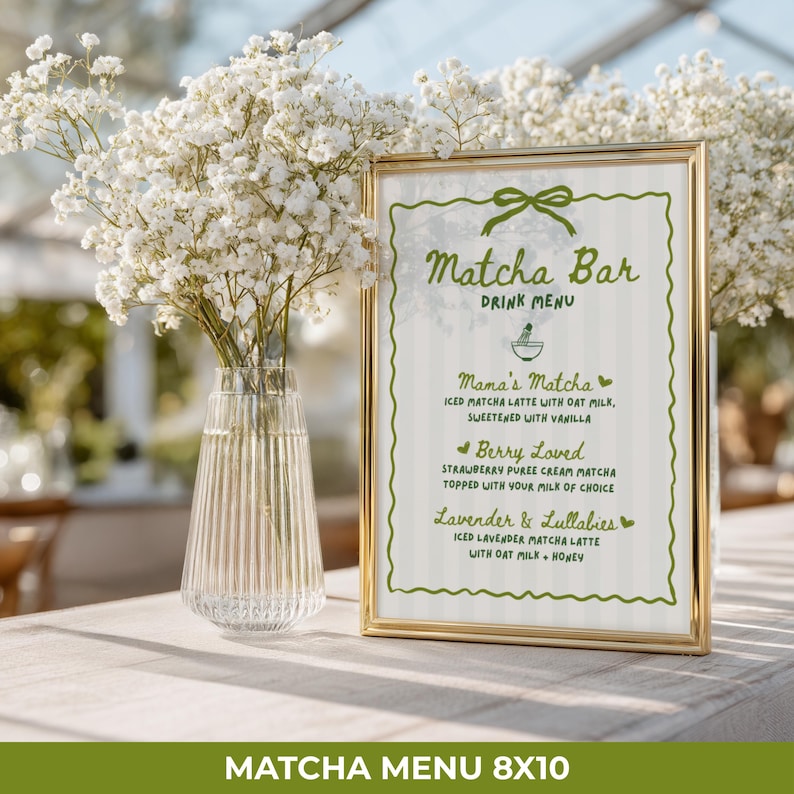 May include: A gold-framed "Matcha Bar" drink menu with a green border and text. The menu lists three matcha latte options: Mama's Matcha, Berry Loved, and Lavender & Lullabies. A vase of white flowers sits to the left. The menu is 8x10 inches.