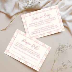 May include: Two baby shower invitation cards with a seashell and starfish design. The cards have text that reads "Books for Baby" and "Diaper Raffle". The cards are light pink and cream colored.