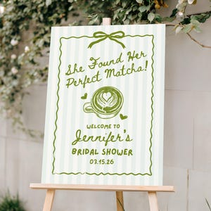 May include: A welcome sign for Jennifer's bridal shower, featuring a green and white striped background. The sign reads "She Found Her Perfect Matcha!" with a matcha latte illustration and the date 03.15.26.