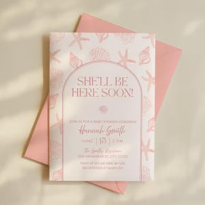 Op de afbeelding: Een uitnodiging voor een babyshower met een roze en wit zeeschelpenontwerp. De uitnodiging luidt "SHE'LL BE HERE SOON!" en bevat details voor Hannah Smith's babyshower, inclusief datum, tijd en locatie.