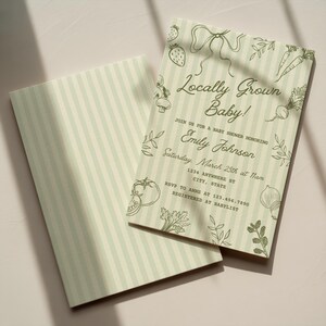 May include: Baby shower invitations with a light green and white striped background. The invitations feature the text "Locally Grown Baby!" and include illustrations of vegetables and fruits. The invitation is for Emily Johnson.