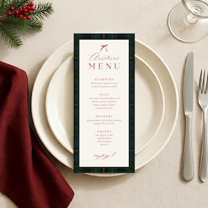 Op de afbeelding: Een kerstmenu met een groen en marineblauw geruite rand ligt op een wit bord, naast bestek en een wijnglas. Het menu heeft een rode strik en de woorden "Christmas MENU" in elegant schrift. Het menu bevat voorgerechten, hoofdgerechten, dessert en drankjes.