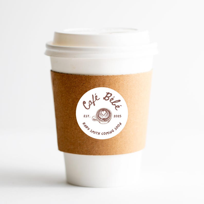 May include: A white paper coffee cup with a brown cardboard sleeve. A round sticker on the cup reads "Caf&eacute; B&eacute;b&eacute;" with a coffee cup design and the text "Baby Smith Coming Soon". The cup has a white lid.