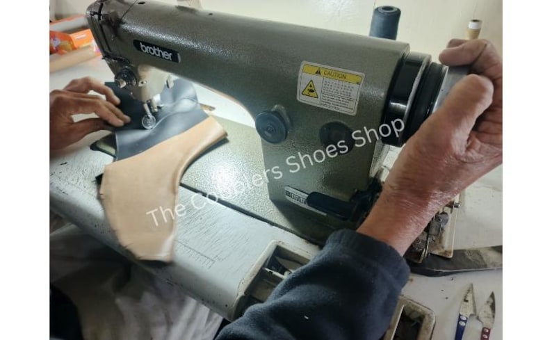 May include: A close-up of a Brother industrial sewing machine in use. The machine is olive green and is stitching together a shoe component. The text "The Couplers Shoes Shop" is visible on the surface.