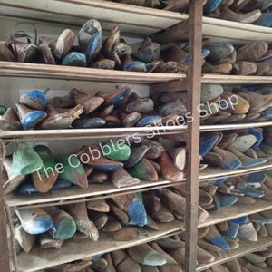 May include: A wooden shelving unit filled with various shoe lasts. The lasts are in different sizes and colors, including blue, green, and brown. The text "The Cobblers Shoes Shop" is visible on the image.