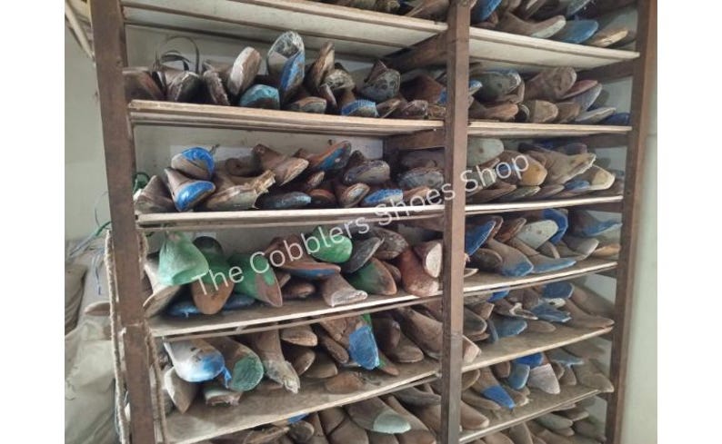 May include: A wooden shelving unit filled with various shoe lasts. The lasts are in different sizes and colors, including blue, green, and brown. The text "The Cobblers Shoes Shop" is visible on the image.