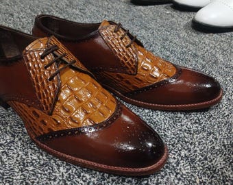 Puede incluir: Un par de zapatos de cuero marrón con un patrón de cocodrilo en la punta. Los zapatos tienen un cierre de cordones y un diseño de punta de ala.