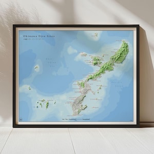 May include: Framed map of Okinawa Dive Sites, featuring a detailed topographical view of the islands. The map shows the East China Sea and Pacific Ocean, with text in English and Japanese. The frame is black.