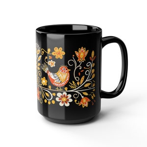 May include: Black ceramic mug with a colorful floral and bird design. The design features a stylized bird with orange, red, and yellow accents, surrounded by yellow, orange, and white flowers and leaves.