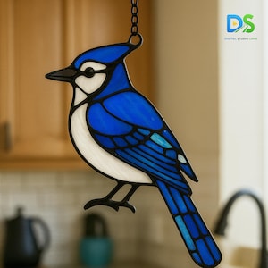 May include: A stained glass blue jay bird suncatcher with black outlines and a chain for hanging. The bird features shades of blue, white, and black, with a detailed design. The Digital Studio Lane logo is visible in the upper right corner.