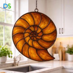 May include: A decorative, hanging nautilus shell made of amber-colored glass with a dark brown metal frame. The shell is suspended from a chain and is illuminated, showcasing its spiral design. The image is set in a kitchen.
