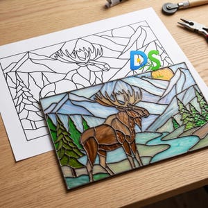 May include: A stained glass panel depicting a moose in a mountain landscape. The panel features shades of brown, blue, green, and yellow. A black and white line drawing of the same image is next to the panel.