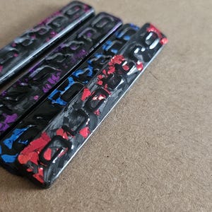 Pode incluir: Quatro objetos retangulares pretos com detalhes coloridos. Os objetos têm um acabamento brilhante e são decorados com padrões roxos, azuis e vermelhos. A palavra "LOGO" é visível em cada objeto.