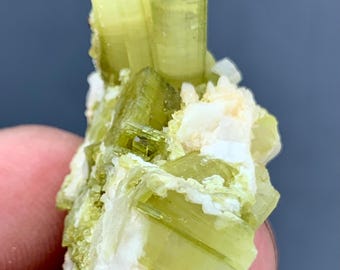 May include: Close-up of a mineral specimen featuring a cluster of light green and yellow crystals. The crystals have a columnar structure with a translucent appearance, and are accented by white and off-white mineral inclusions.