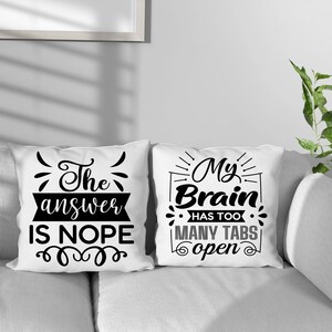 May include: Two white throw pillows with black text. One pillow reads "The answer is NOPE" and the other says "My Brain has too many tabs open". The pillows are on a white couch.