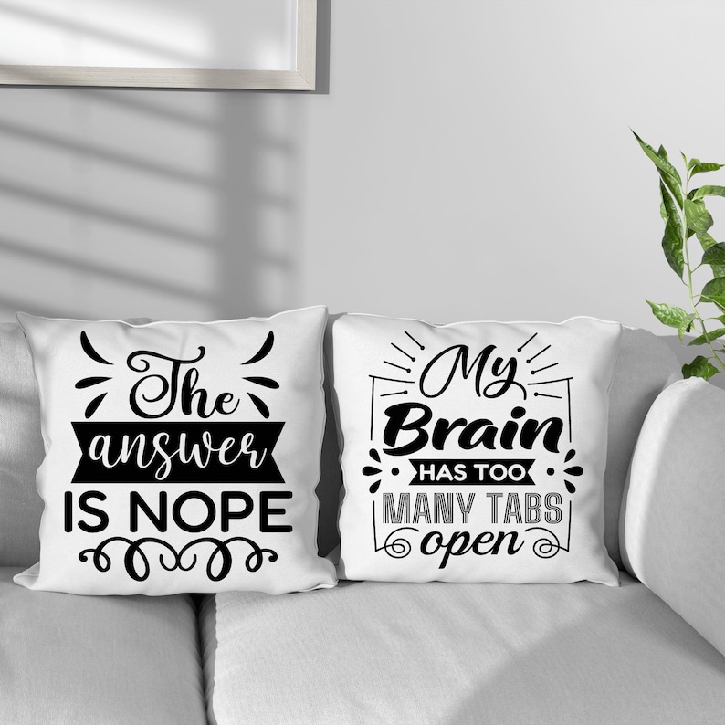 May include: Two white throw pillows with black text. One pillow reads "The answer is NOPE" and the other says "My Brain has too many tabs open". The pillows are on a white couch.