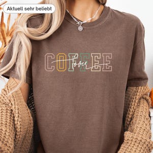 May include: A brown t-shirt with the text "COFFEE lover" in a multi-colored design. The word "COFFEE" is in a block letter style with yellow, green, and pink accents. The word "lover" is in a cursive font.