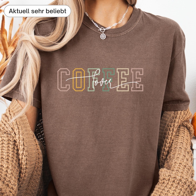 May include: A brown t-shirt with the text "COFFEE lover" in a multi-colored design. The word "COFFEE" is in a block letter style with yellow, green, and pink accents. The word "lover" is in a cursive font.
