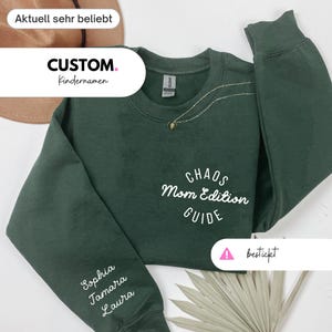 Könnte beinhalten: Ein dunkelgrünes Sweatshirt mit den Worten "CHAOS Mom Edition GUIDE" in weißer Schrift. Der Ärmel hat die Namen "Sophia Tamara Laura" in weißer Schrift. Das Sweatshirt hat auch eine goldene Halskette.