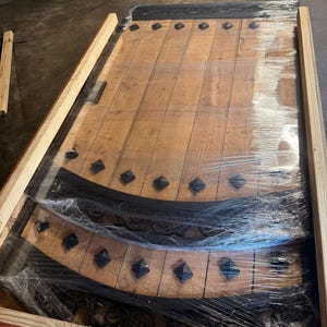 May include: Wooden door panels with decorative black metal accents and diamond-shaped studs. The panels are wrapped in clear plastic and are inside a wooden crate. The wood has a natural finish.