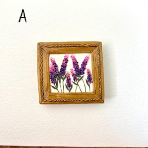 May include: A small, square framed artwork featuring lavender flowers in shades of purple and pink against a white background. The frame is a warm, light brown color with a textured rope-like design. The letter "A" is in the upper left corner.