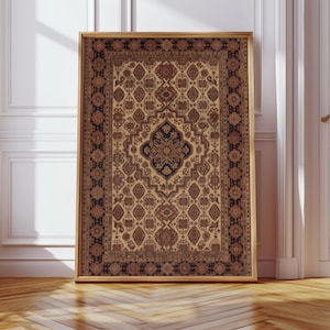 May include: A framed rug with a detailed, traditional pattern. The rug's design includes a central medallion and repeating motifs in beige, brown, and navy. The frame is gold-toned, and the rug is displayed against a white wall, with a wooden floor.