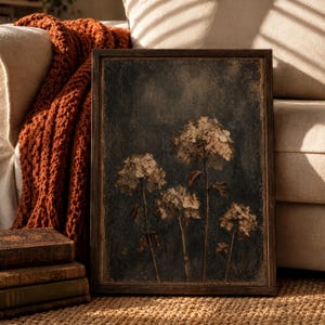 May include: A rectangular framed wall art piece featuring a dark, textured background with four muted, sepia-toned hydrangea flower clusters on thin stems. The frame is a dark wood finish, and the artwork displays a weathered, aged aesthetic.