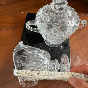 May include: Clear crystal creamer and sugar bowl set. The creamer measures approximately 4 inches in length. The sugar bowl has a lid and two handles. Both pieces have a cut glass design.