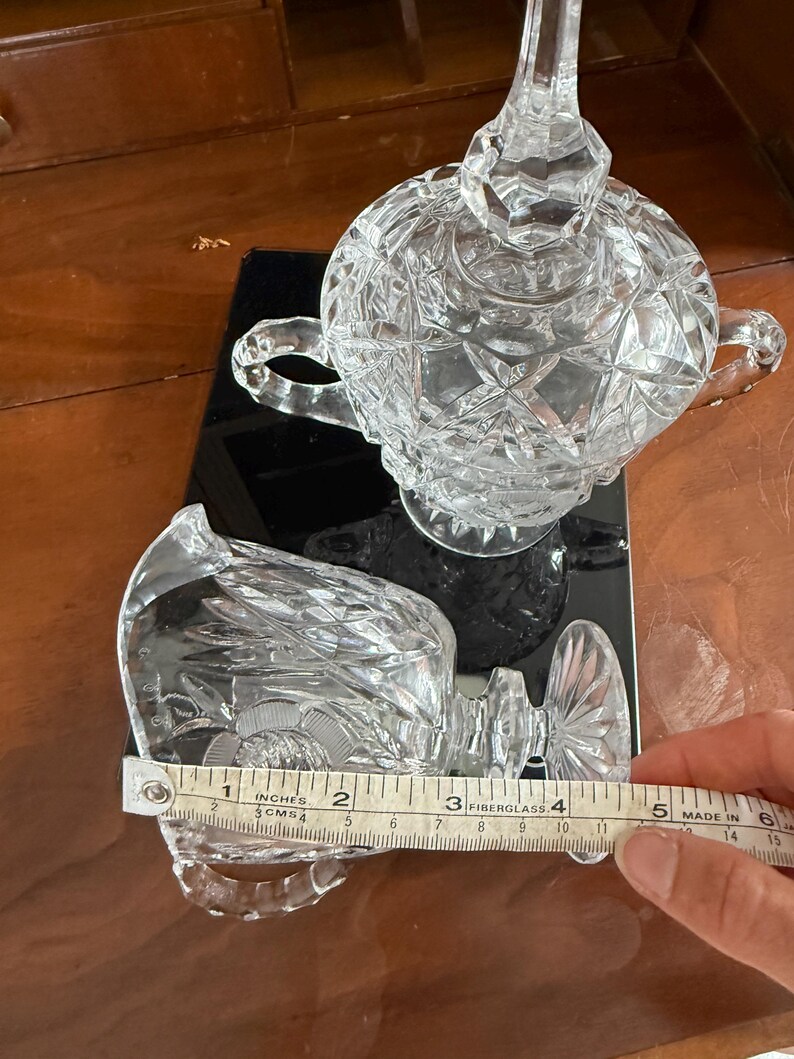May include: Clear crystal creamer and sugar bowl set. The creamer measures approximately 4 inches in length. The sugar bowl has a lid and two handles. Both pieces have a cut glass design.